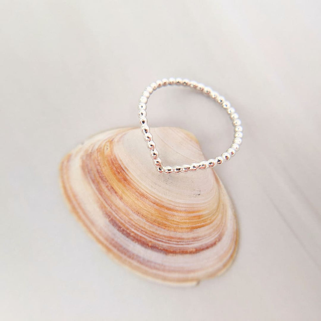 Sterling silver Beaded Droplet Midi Boho Ring: A close-up photo of a handcrafted sterling silver V-shaped ring with a delicate beaded design, resting on a pink and orange shell.