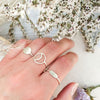 A woman's hand with 3 sterling silver rings: one is a delicate ring featuring an embossed twig branch design, one is a crescent moon design, and one is a hammered full moon design.
