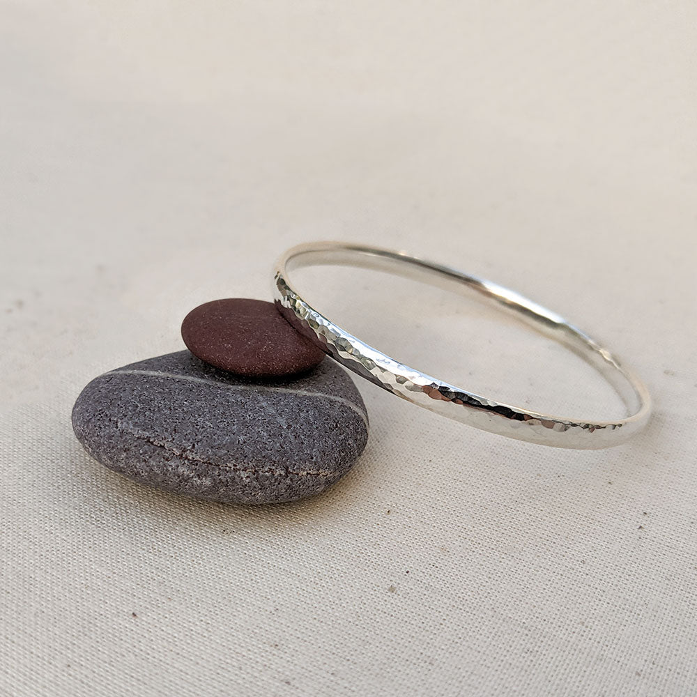 Chunky sterling silver round bangle with hammered texture design resting on purple and grey stones