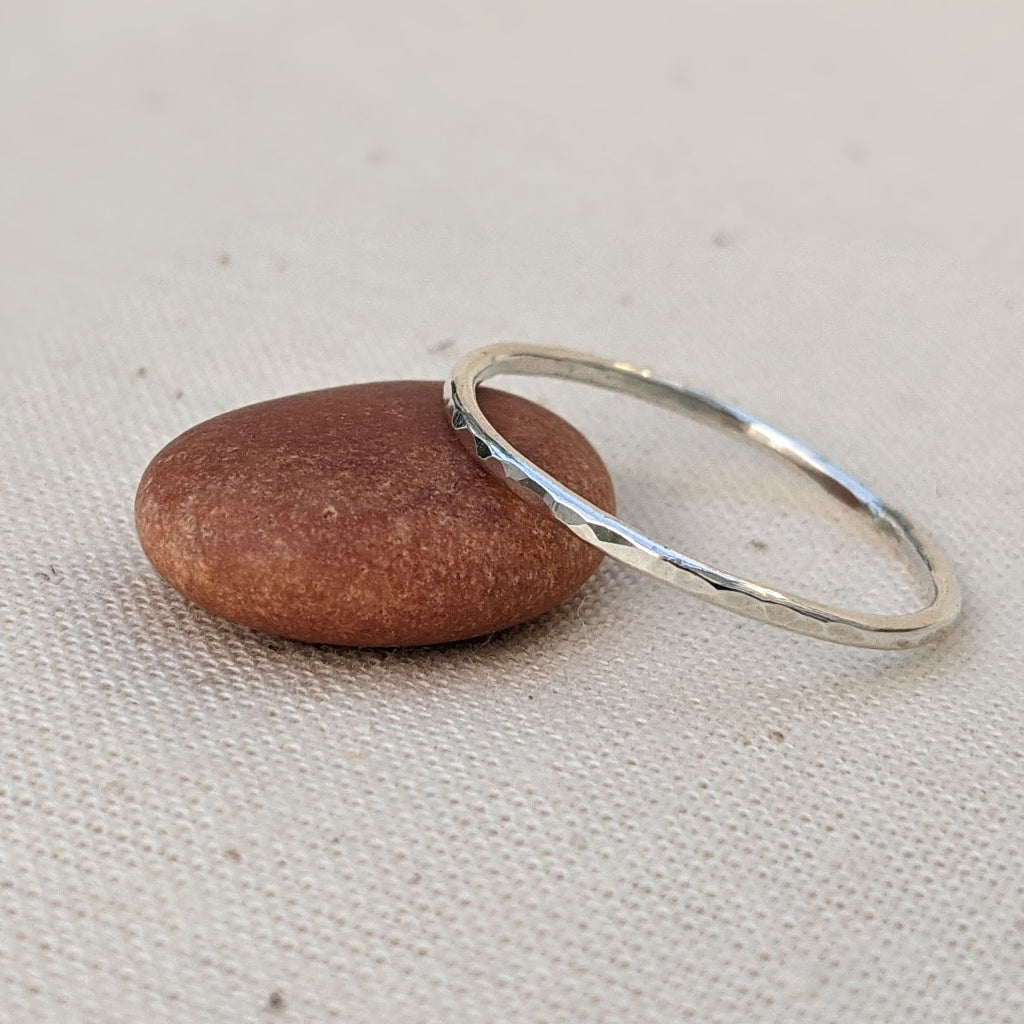 Thin sterling silver hammered round stacking ring resting on stone