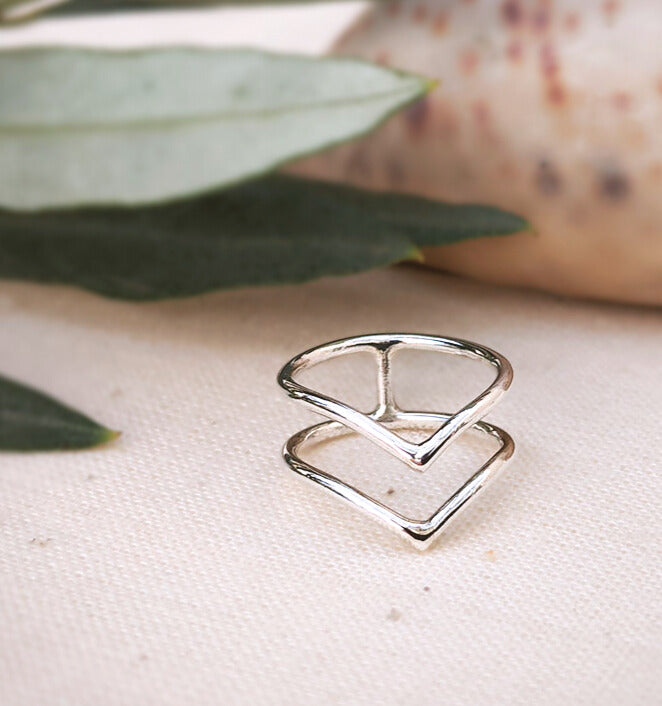 Front view of sterling silver midi boho ring in connected double V-shaped design, with green leaves in background