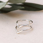 Side view of sterling silver midi boho ring in connected double V-shaped design, with green leaves in background