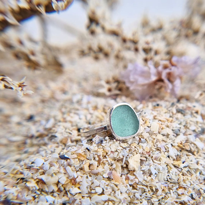 Close up photo of a turquoise sea glass ring with hammered sterling silver band, showcasing a vibrant turquoise hue reminiscent of ocean depths.