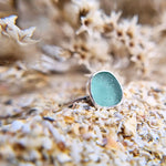 Close up photo of a turquoise sea glass ring with hammered sterling silver band, showcasing a vibrant turquoise hue reminiscent of ocean depths.